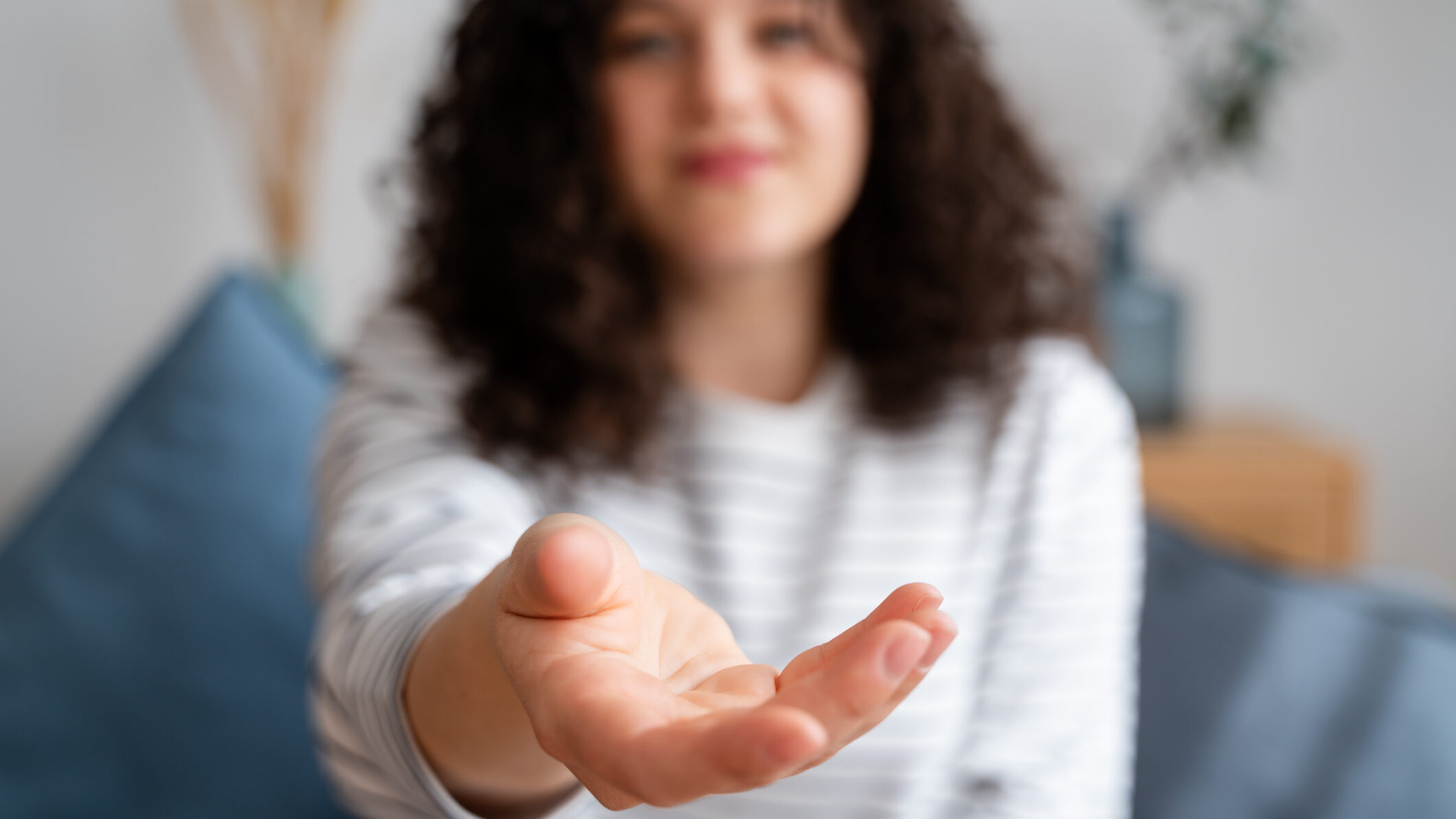 Close-up of a woman's open hand extended towards the camera with a blurred background, conveying assistance, offering, or invitation